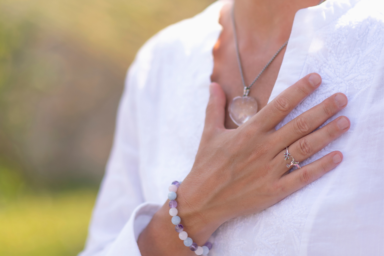 A woman with her hand on her chest, symbolizing gratitude and self-value, wearing a necklace and bracelet that reflect inner strength. Kimberly Brenner, Chicago Marriage Coach, helps women embrace their true worth.