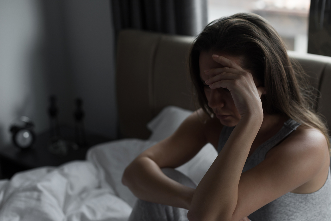 A woman sitting on a bed with her hand on her forehead, symbolizing the emotional struggle of facing an unhappy marriage. Kimberly Brenner, Chicago Marriage Coach, guides women toward clarity and empowered decisions.